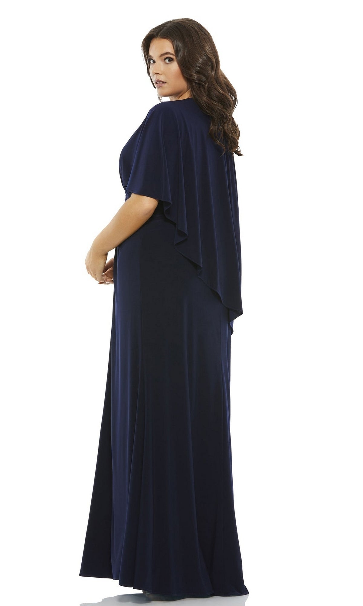 A woman with long brown hair models the Long Plus-Size Prom Dress 67929 by Mac Duggal, featuring cape sleeves and a floor-length design, as she stands looking over her shoulder.